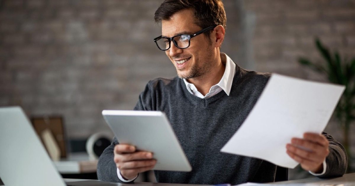Profissional analisando documento fiscal e tablet, conferindo os campos de IBS e CBS na emissão da NF-e