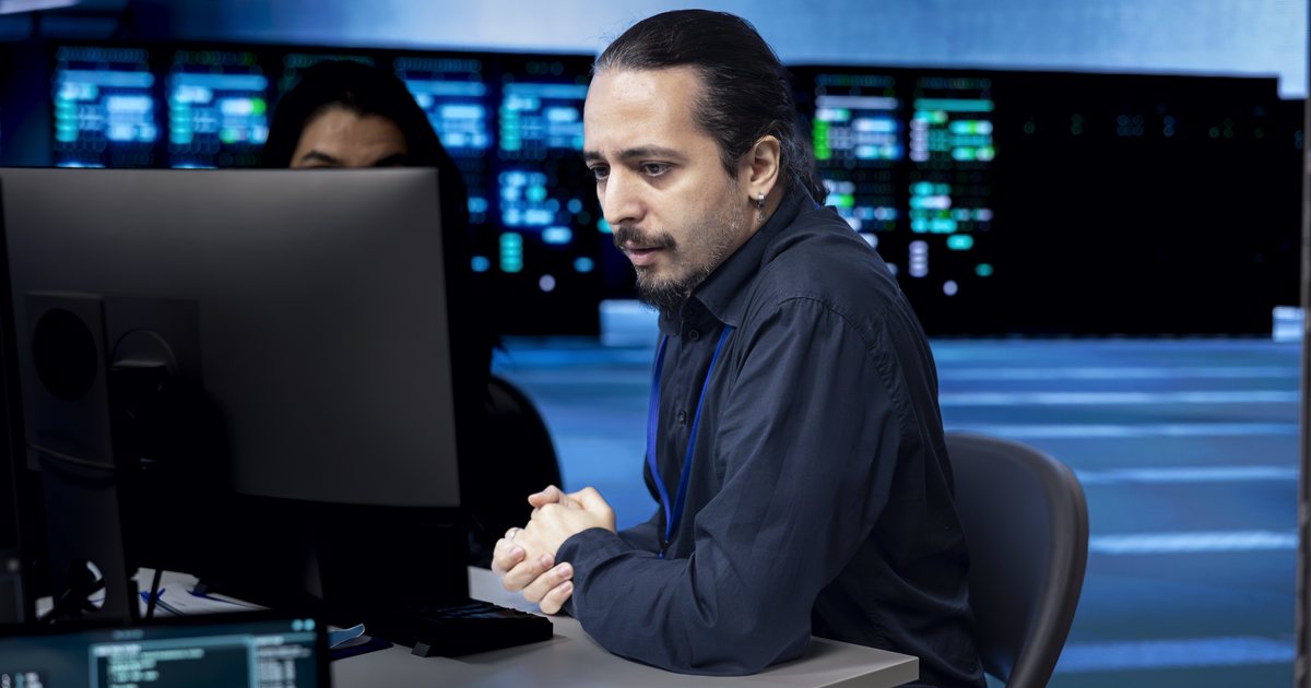 Analista de TI acompanhando o monitor numa sala com servidores ao fundo
