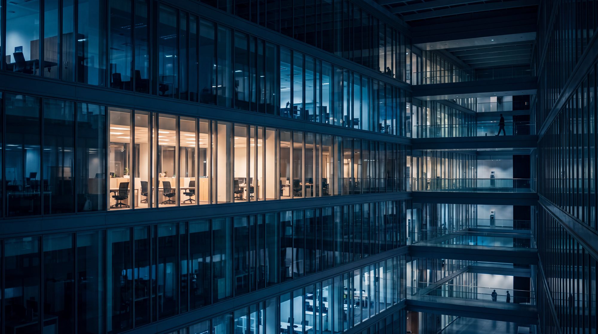 Prédio corporativo à noite visto por dentro, com andares e salas iluminados